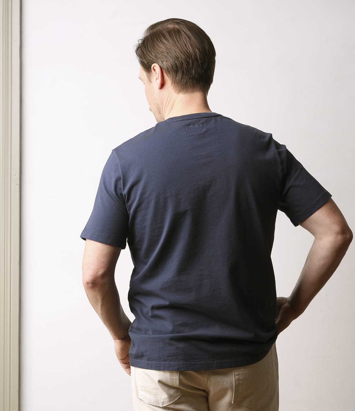 A man with short brown hair, seen from behind, wears the Best Made Co Standard Pocket T-Shirt in navy and light-colored pants against a plain, light background.