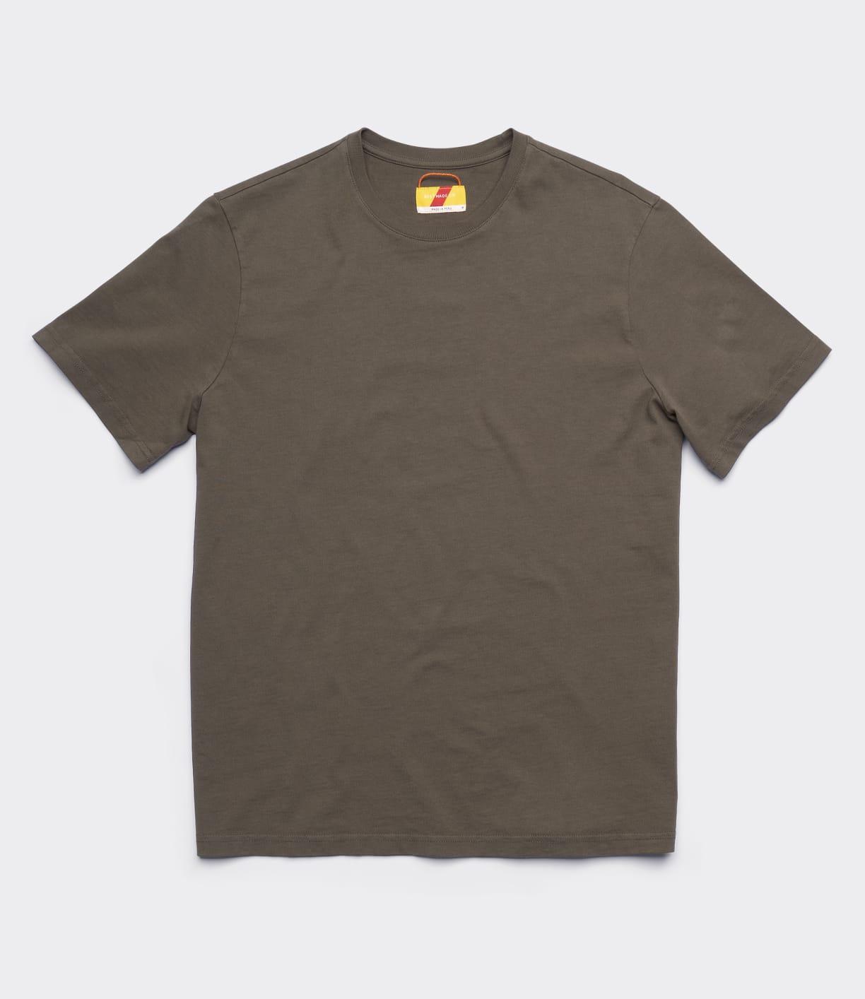 The Best Made Co. Standard T-Shirt Field Drab is a solid olive green, garment-dyed short-sleeve crew neck made from soft Peruvian tangüis cotton, shown flat on white with a small colorful design on the inner neck tag.