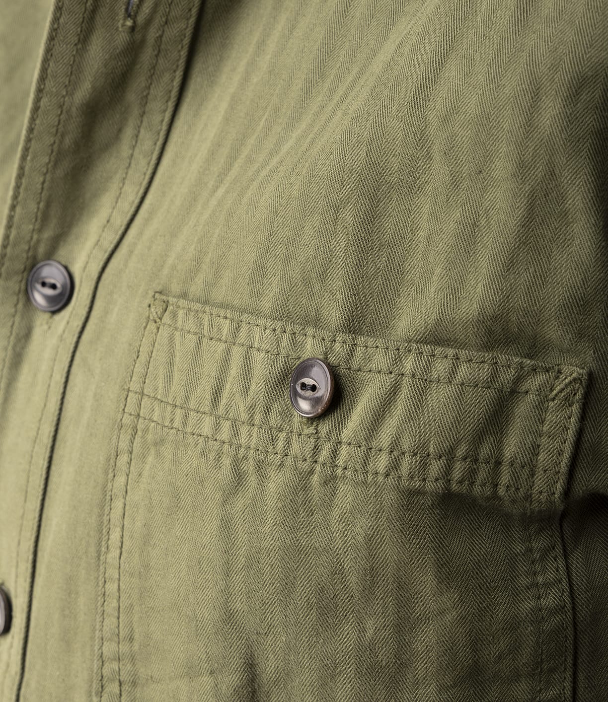 Close-up of the Best Made Co. Cotton-Linen Workshirt in Olive Drab, highlighting its herringbone pattern, buttoned chest pocket, and front buttons.