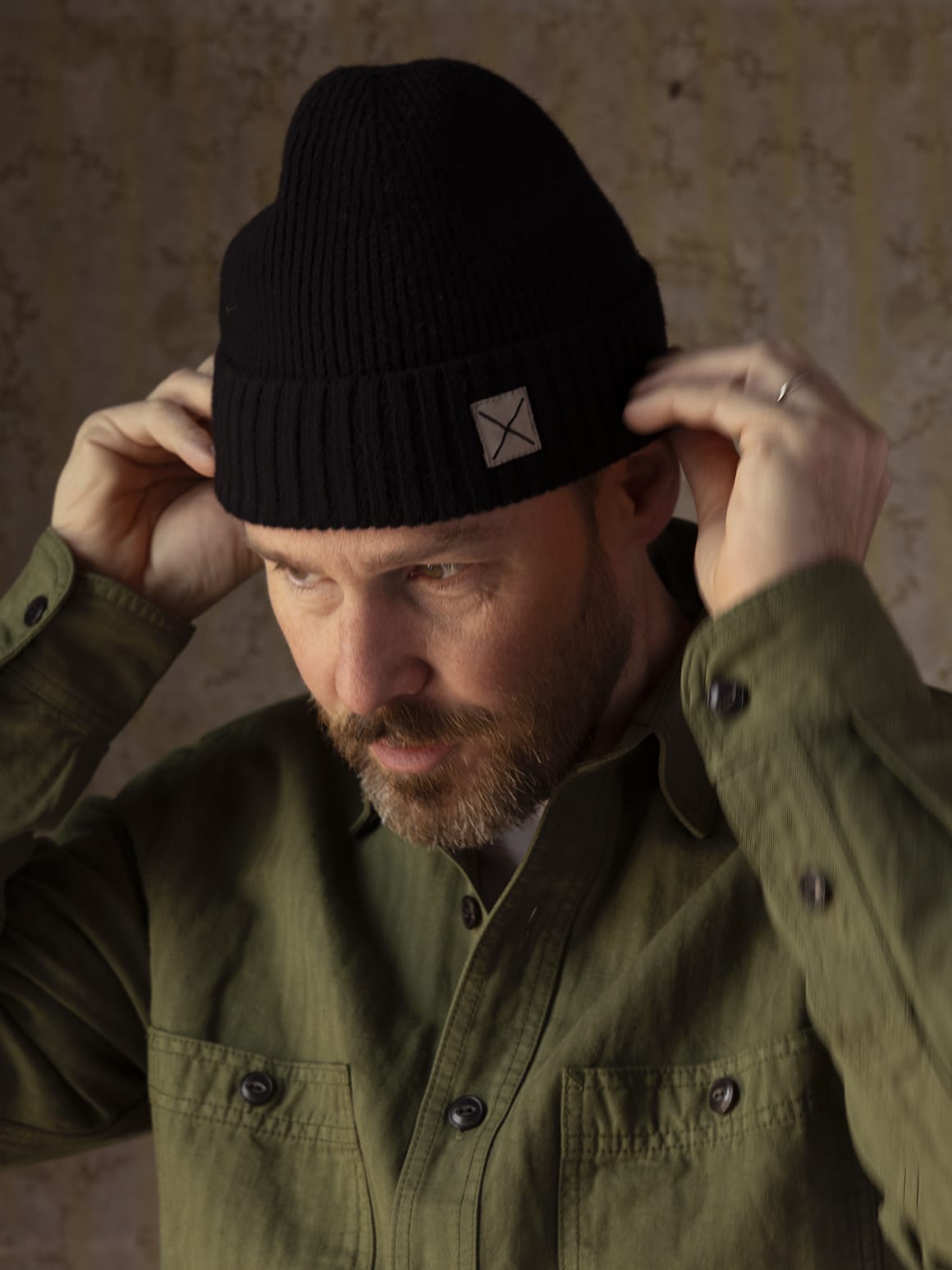 A man adjusting a black lambswool Cap of Courage featuring a small square patch with an X on the cuff.