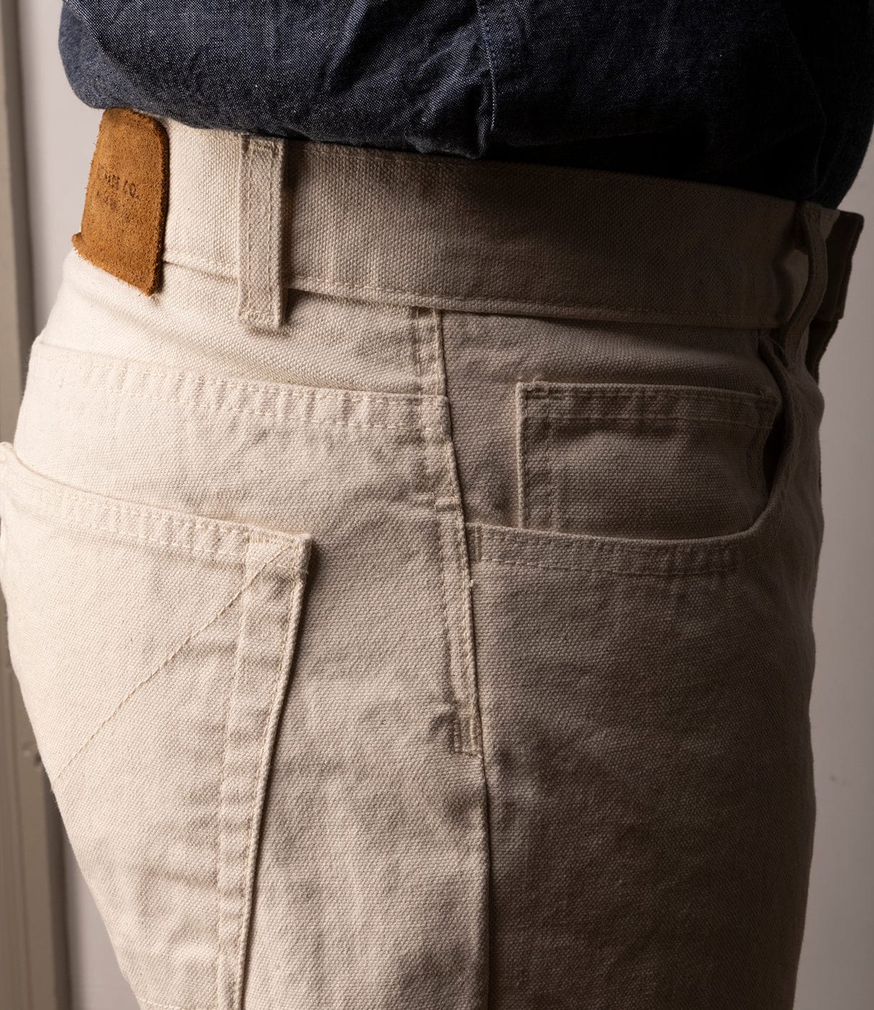Close-up side view of a person wearing Best Made Co's Standard 5-Pocket Pant M2 Undyed, made from heavyweight cotton with a brown leather waistband patch. The pants feature classic straight leg, visible stitching, and pocket details.