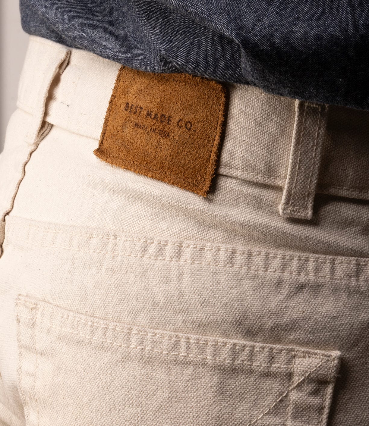 Close-up of the back of the Standard 5-Pocket Pant M2 Undyed by Best Made Co, showing a brown leather patch above the pocket. The wearer’s dark shirt is partly visible. Made from heavyweight cotton for lasting comfort.