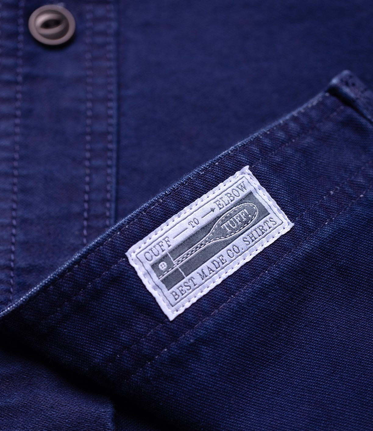 A close-up of the Best Made Co Indigo Moleskin Work Shirt shows a white pocket label that reads "Cuff to Elbow Tough, Best Made Co. Shirts" with a measuring tape illustration.