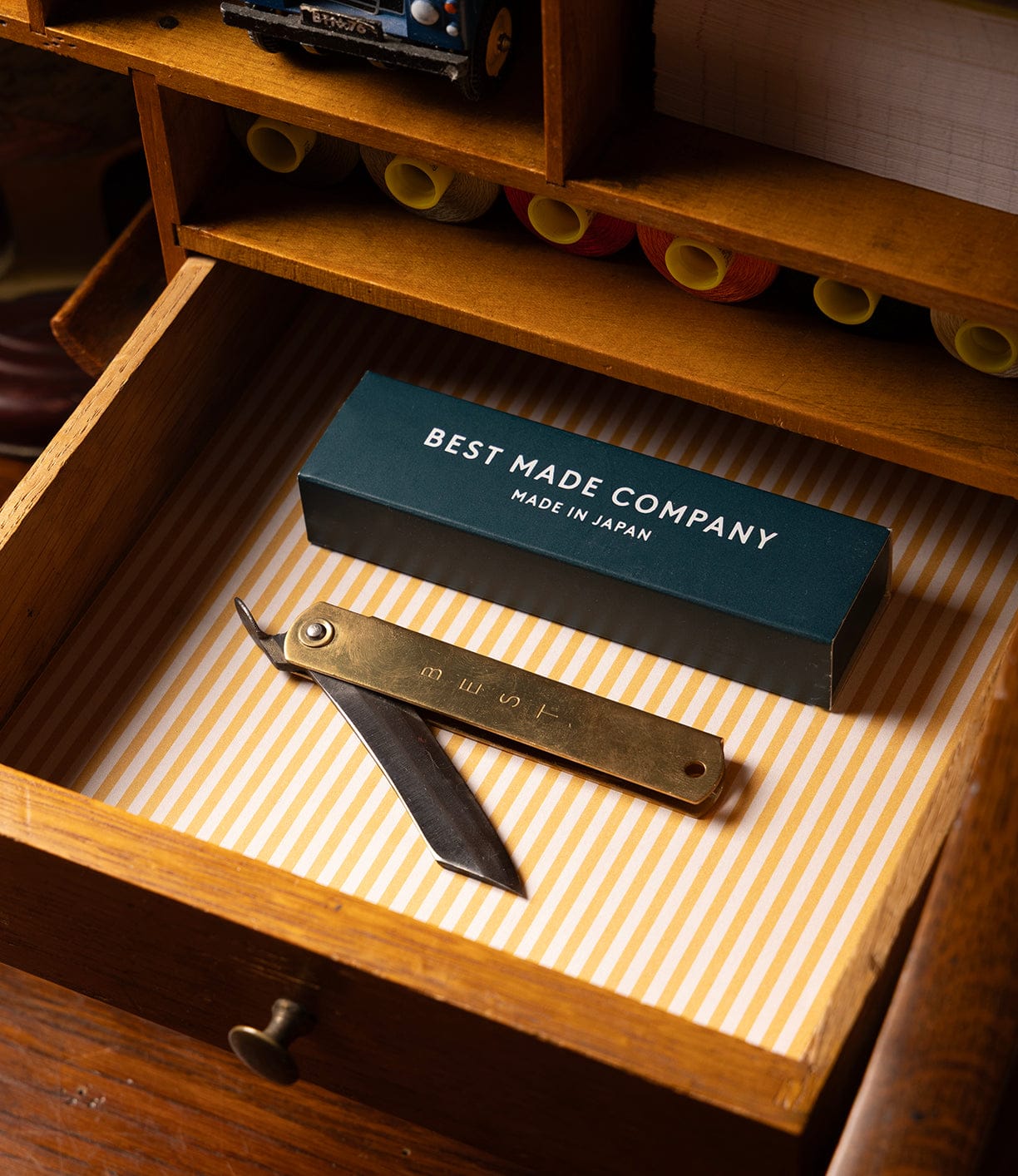 An open wooden drawer reveals a Little Doctor Stainless Wood knife by Best Made Co and a dark box labeled Best Made Company Made in Japan, both resting on striped paper inside.