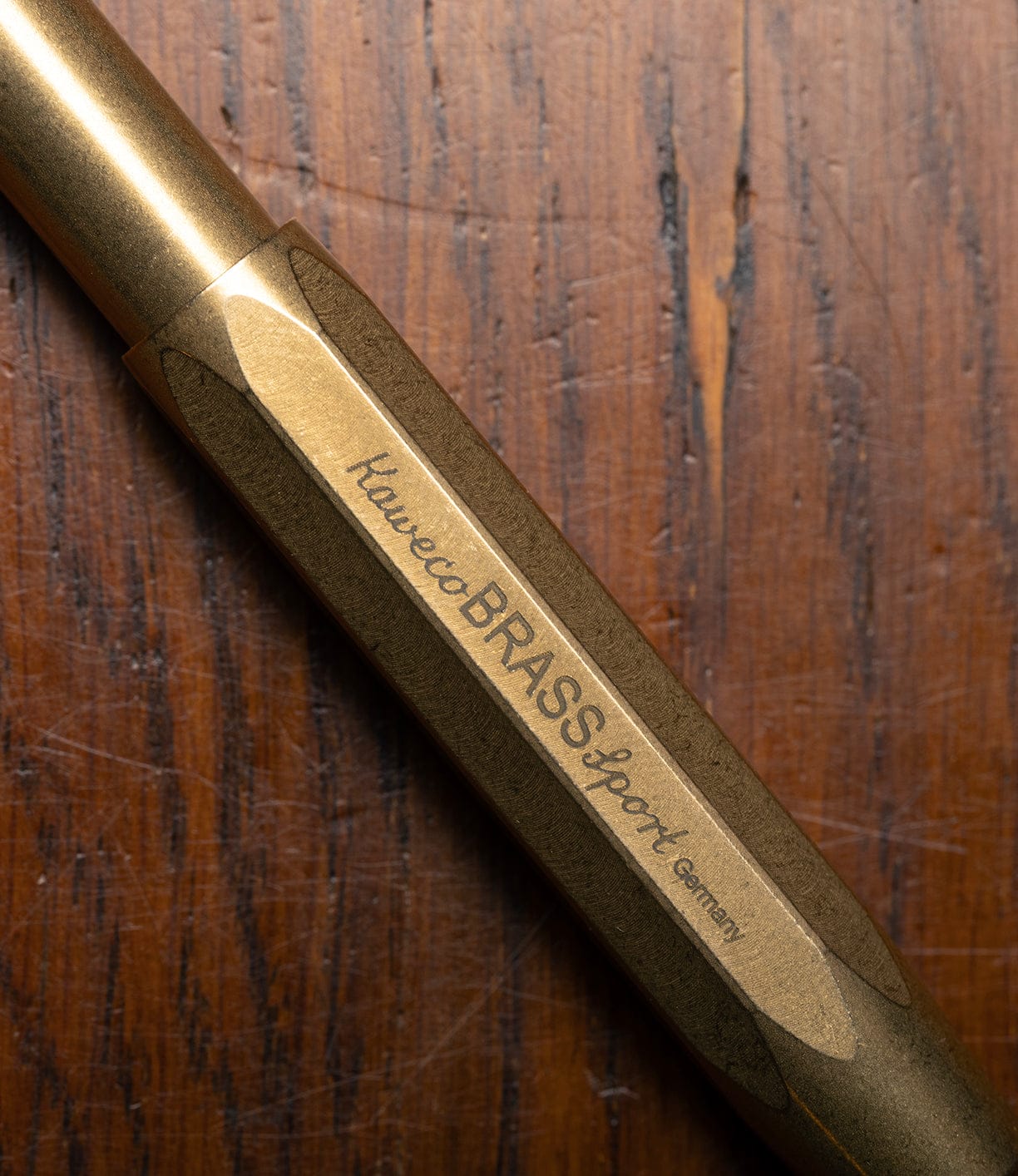 A close-up of a metallic Best Made Co. Kaweco Sport brass pocket pen, engraved with "Germany," rests on wood; this compact pen uses a G2 rollerball refill for smooth writing.