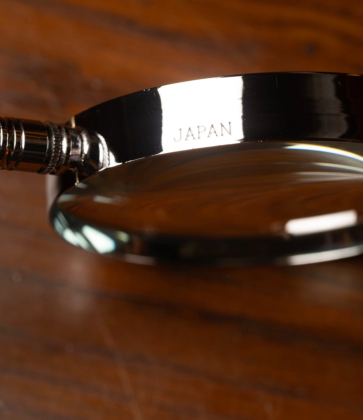 A close-up of the Japanese Magnifying Glass by Best Made Co., featuring a metal frame engraved with JAPAN, set on a wooden surface.