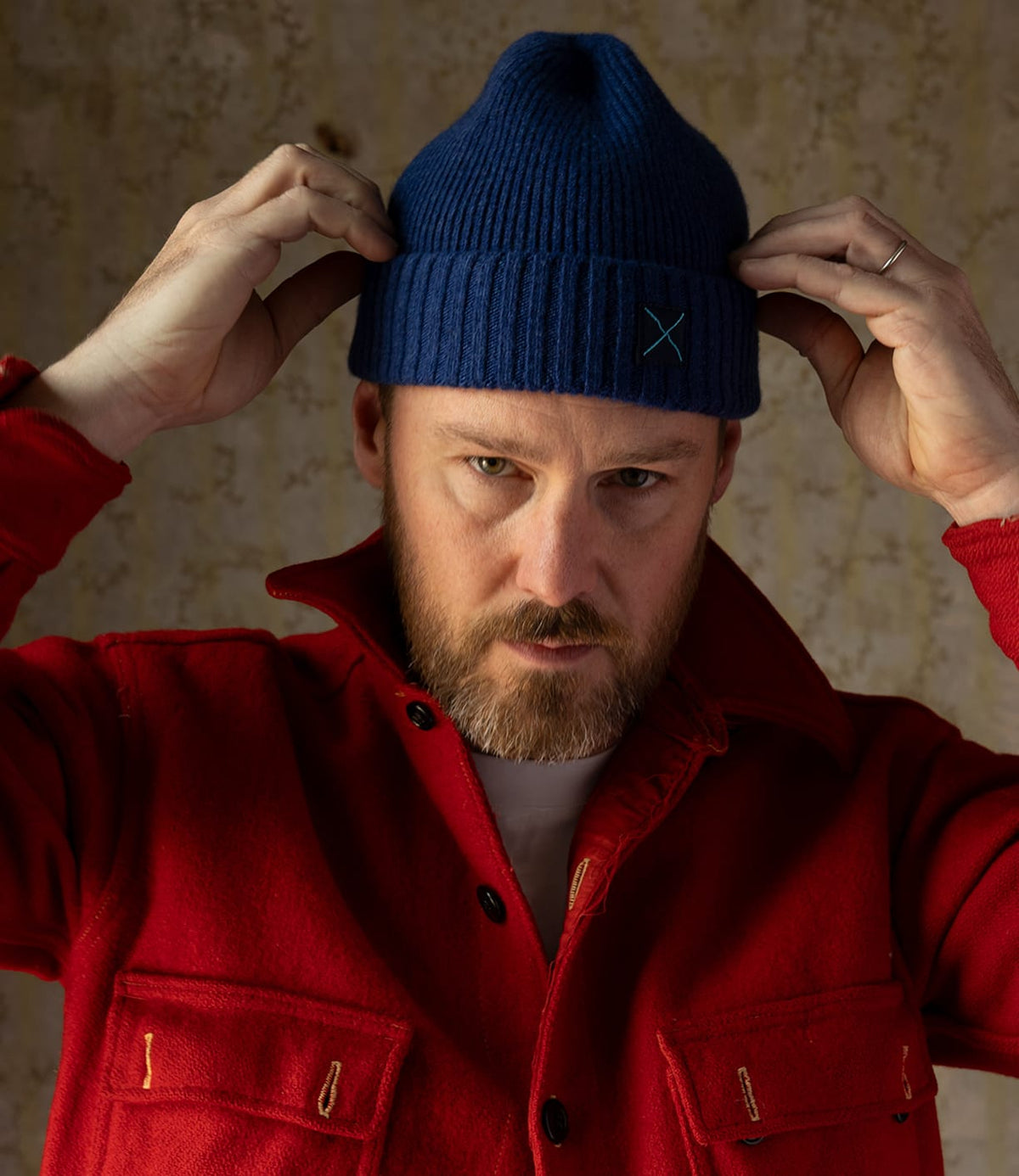 A man wearing a blue ribbed lambswool Best Made Co. Cap of Courage featuring a small teal embroidered X on the cuff.