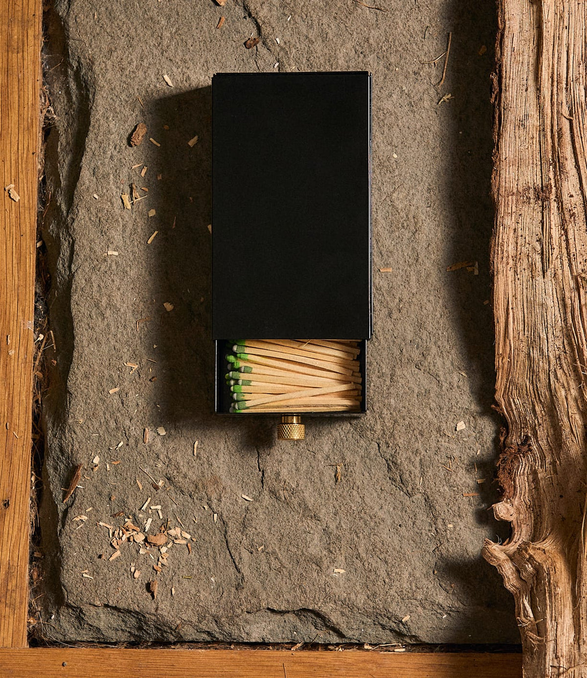 A black rectangular Sliding Match Safe Black by Best Made Co., partially open to reveal strike-anywhere matches with green tips, resting on a stone surface.