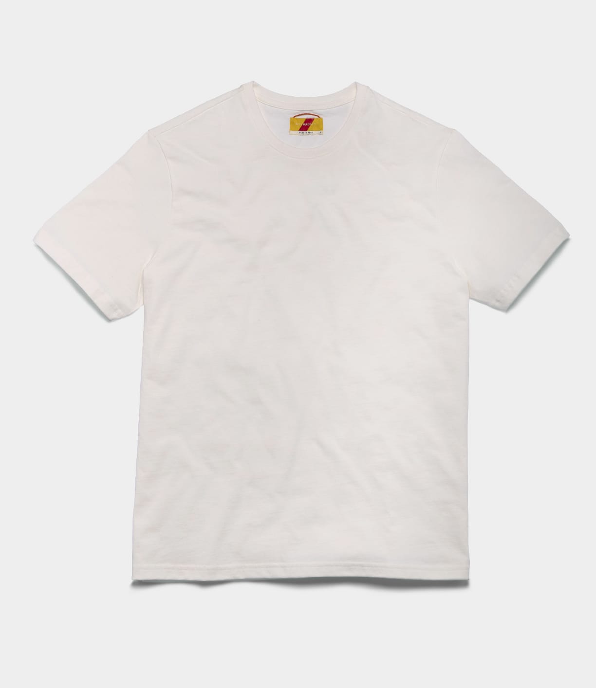 The Best Made Co. Standard T-Shirt Undyed, made from soft Peruvian tangüis cotton, is shown laid flat on a white background with a small colorful tag at the inside neckline.