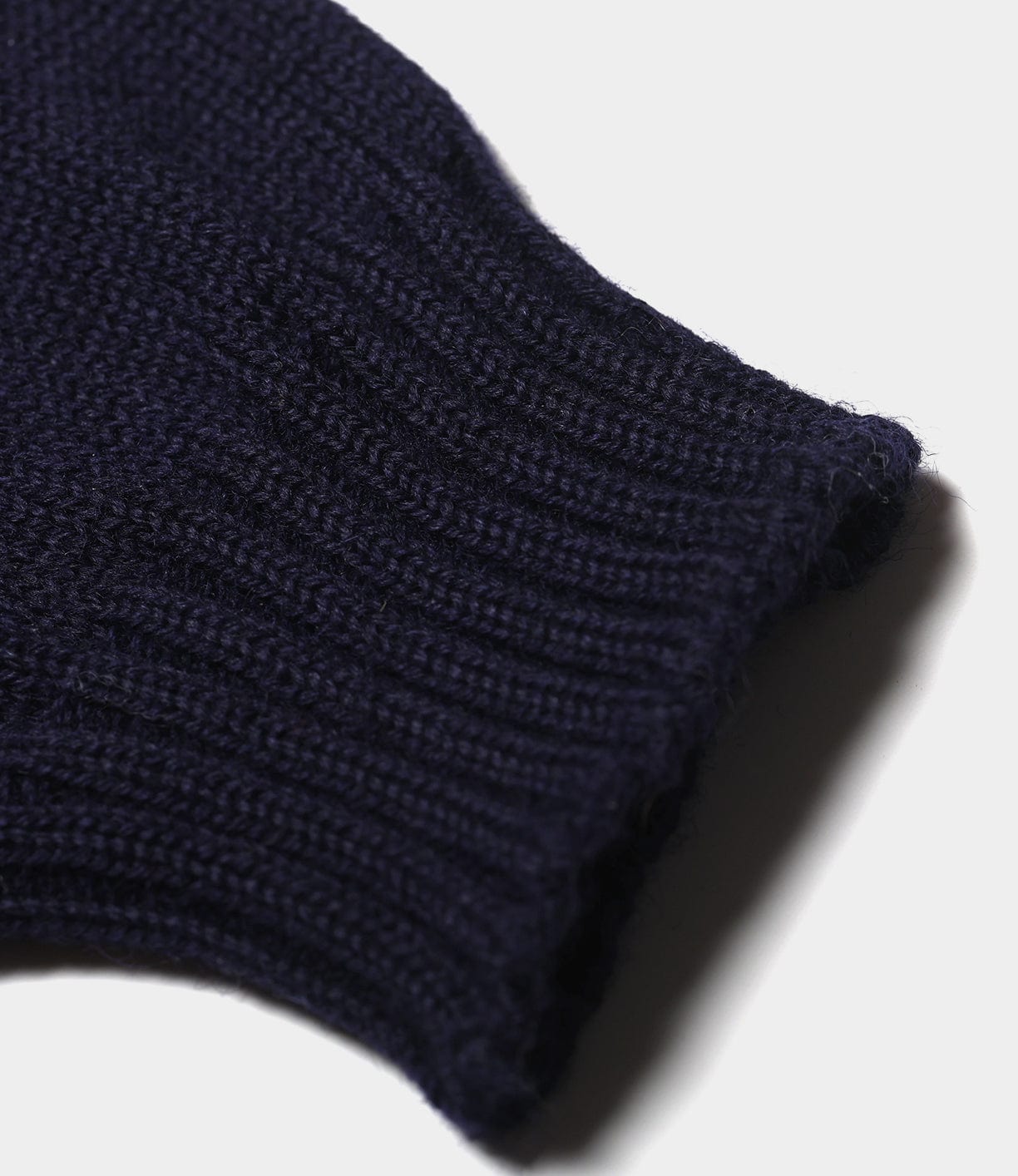 A close-up of a dark navy blue Guernsey Sweater by Best Made Co. shows the ribbed cuff and seamless British wool texture against a white background, highlighting its traditional knitted detail.