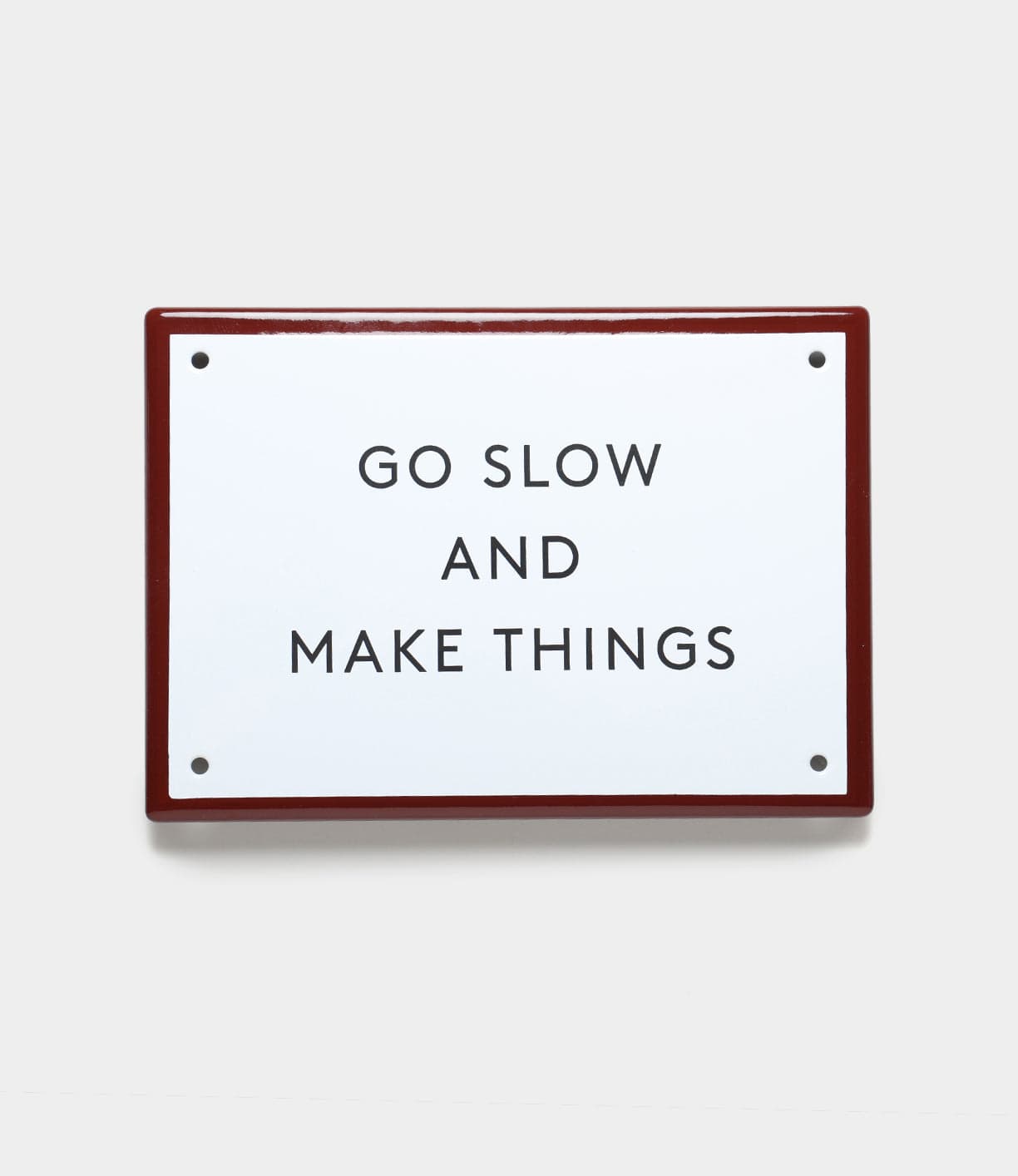 The “Go Slow” Enamel Steel Sign by Best Made Co. features black uppercase text on white enamel with a red border—durable wall decor for any space.
