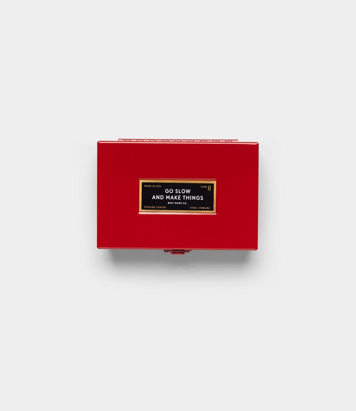 A rectangular red Best Made Co Type 6 Strongbox, Go Slow Edition, features a black and gold “GO SLOW AND MAKE THINGS” label on top, centered against a plain light gray background.