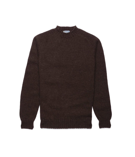 A man with light brown hair and a mustache stands indoors, wearing the Best Made Co. Black Sheep Sweater over a collared shirt and dark jeans. He faces the camera with a neutral expression, framed by dark wood panels and striped wallpaper.