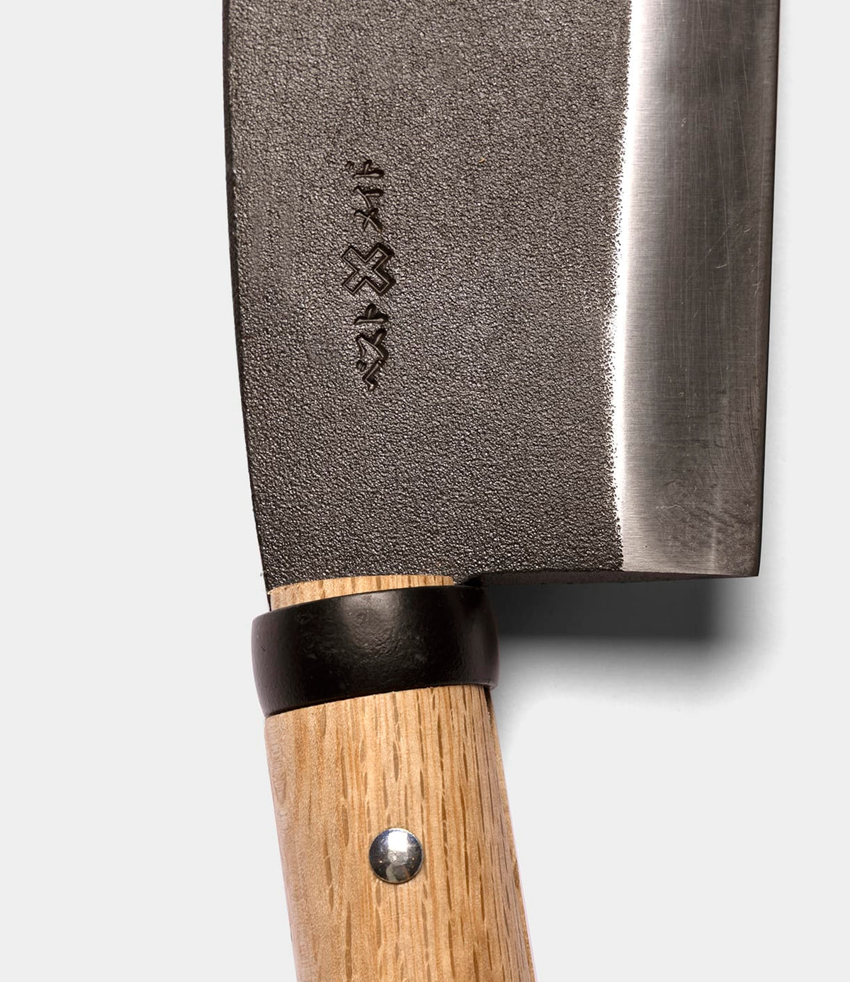 Close-up of the Azuma Hatchet by Best Made Co., showcasing its wooden handle with a metal rivet and an engraved design on the blade near the handle, echoing the traditional style of Japanese carbon steel hatchets, set against a plain light background.