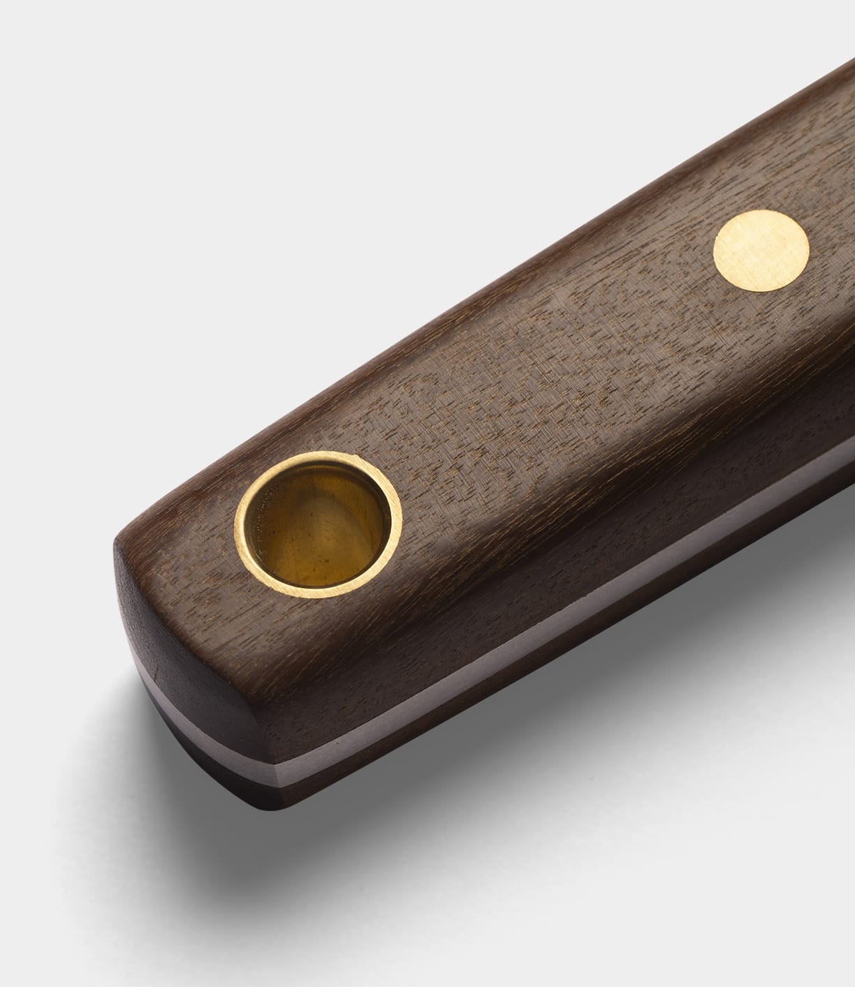 A close-up of the Best Made Co. Sailor’s Knife handle, crafted from rich Brazilian Teak, showcases its smooth finish with a round brass inlay and a circular brass-lined hole on the surface. The design exudes warmth and durability, set against a plain, light-colored background.