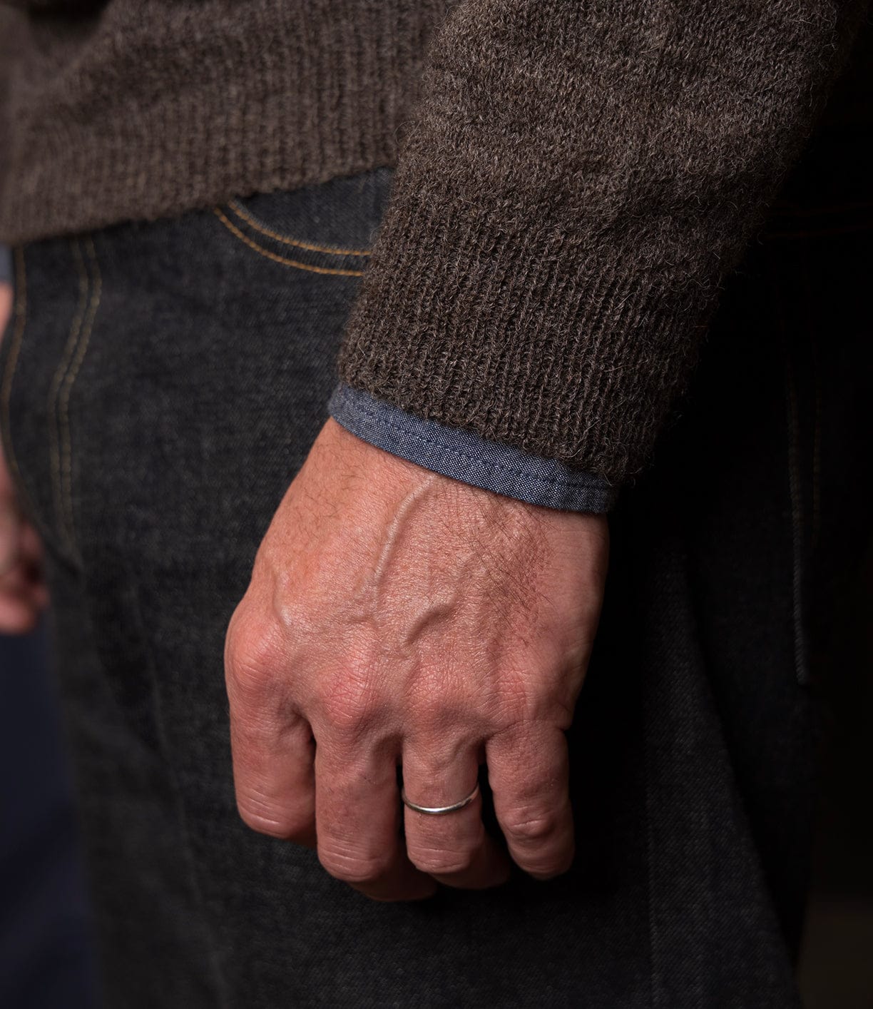 A close-up of a hand with a simple silver ring on the finger, wearing dark jeans and the lightweight 5-Gauge Shetland Sweater from Best Made Co.