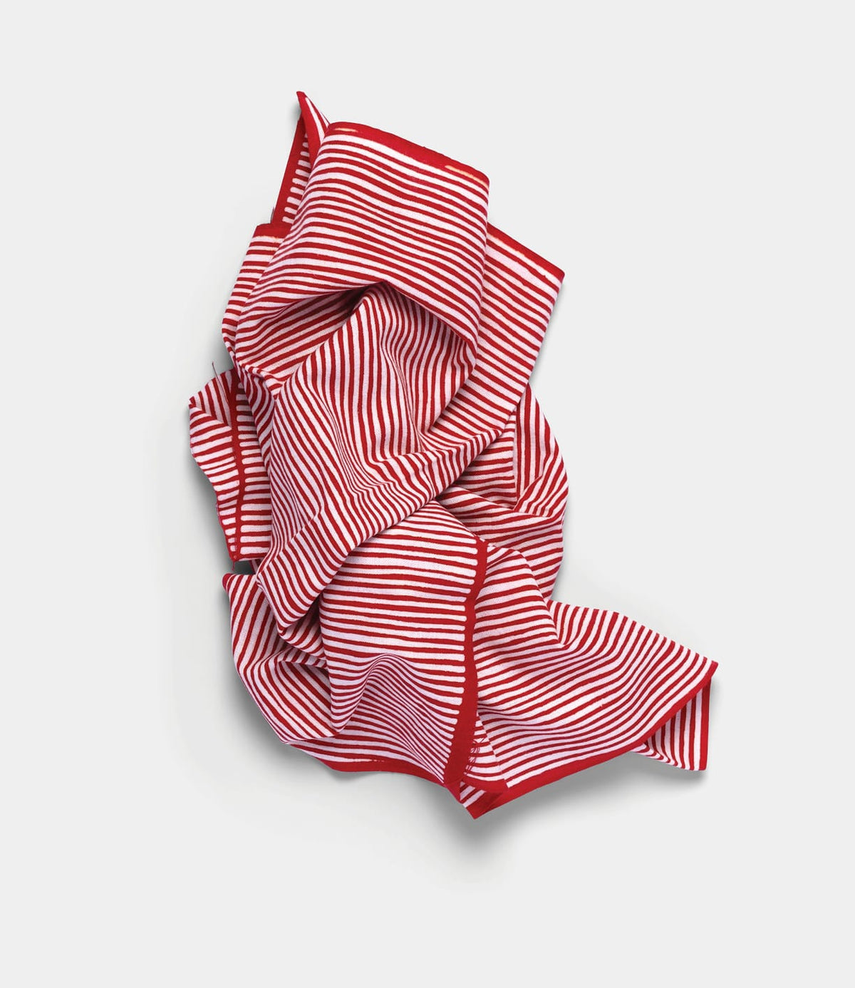 A Yoroke-Jima Tenugui by Best Made Co. with thin horizontal stripes and red edging lies crumpled on a plain, light gray background, showcasing the traditional Japanese hand-dyed chusen technique.