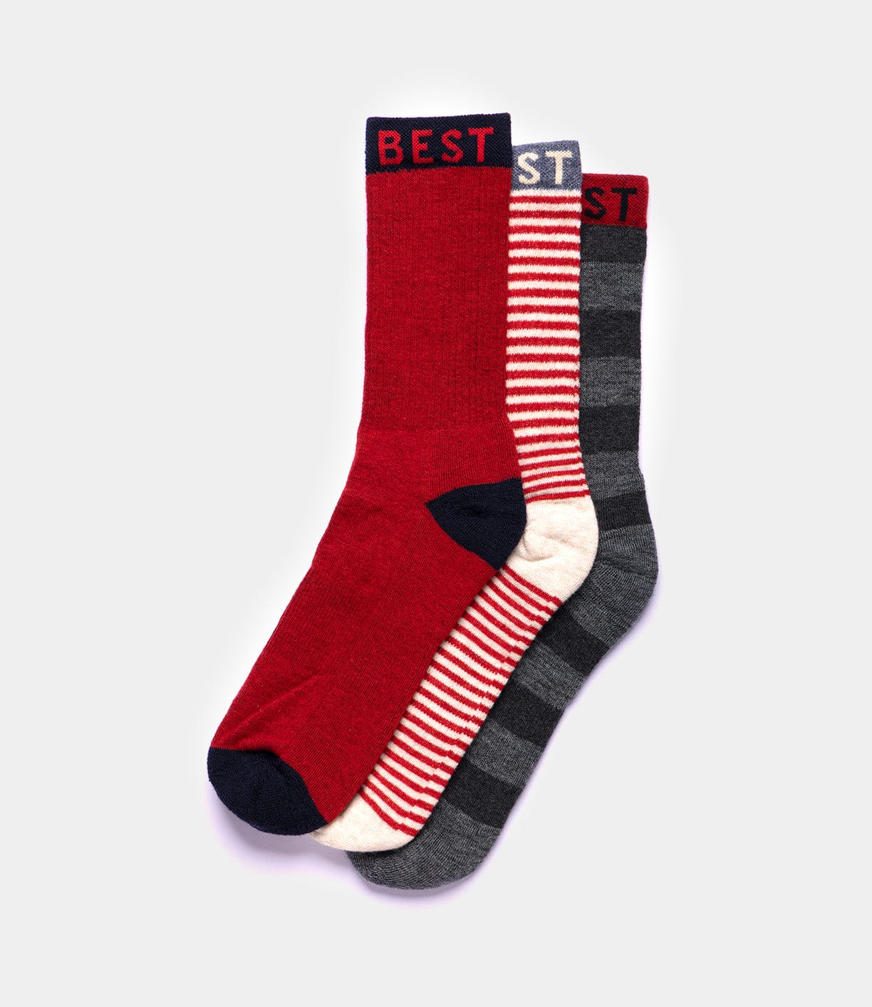 Three pairs of Standard Wool Socks by Best Made Co: one solid red with navy toe and cuff labeled BEST, one with red and white stripes, and one with dark and light gray stripes with a red cuff labeled BEST.