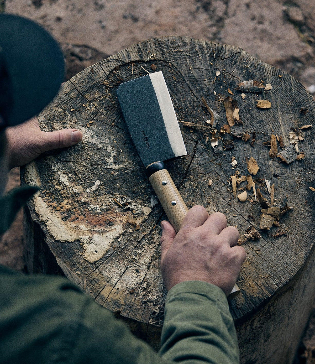 A person holding a compact Best Made Co. Azuma Hatchet with a wooden handle over a worn tree stump, surrounded by wood chips and bark, embodies the rugged functionality of this high-carbon steel tool.