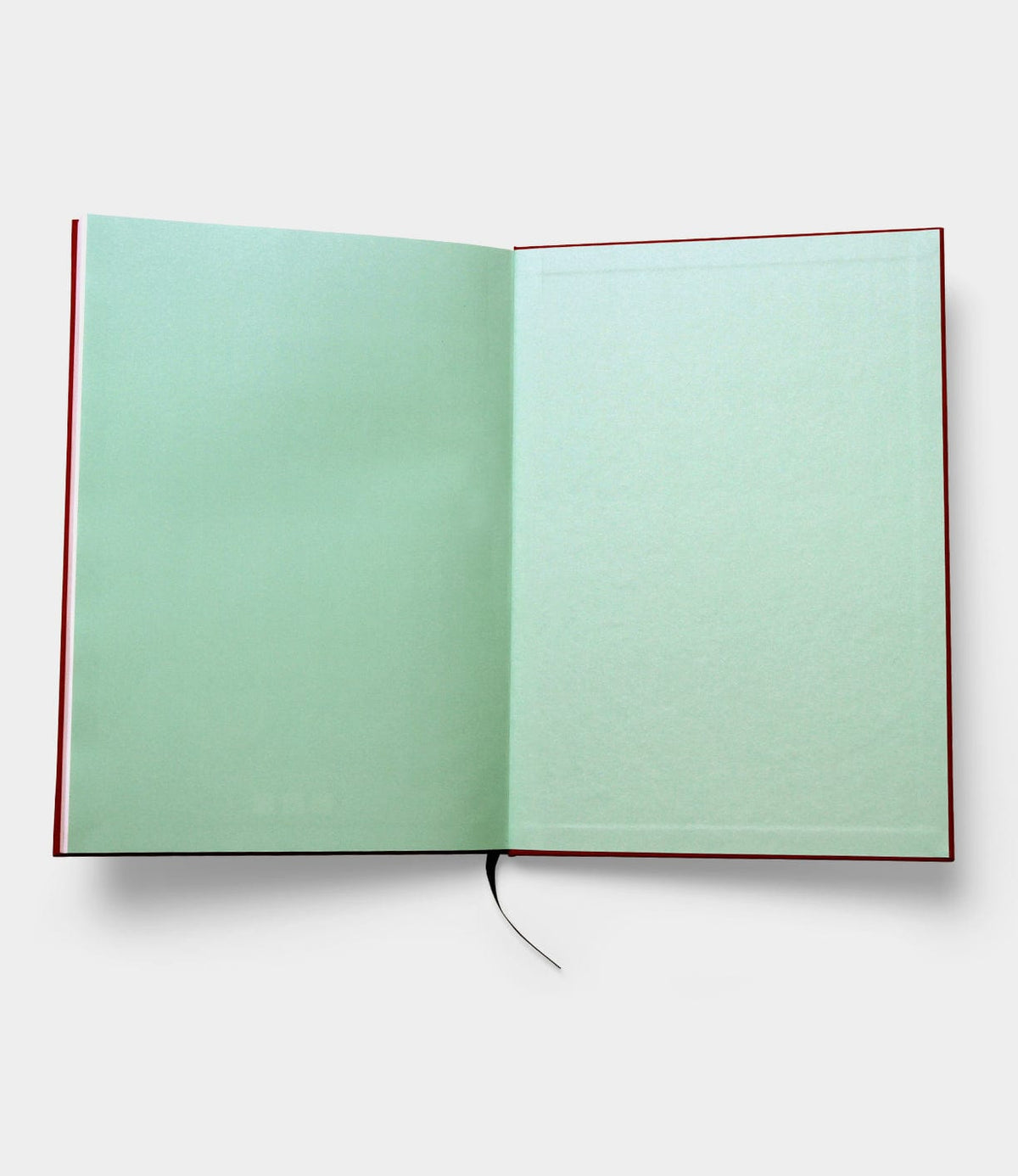 The S.B.T. Max Cloth-Bound Notebook by Best Made Co. features pale green blank pages and a black ribbon bookmark, elegantly complementing its open, cloth-bound hardcover design as it lies flat on a white surface.
