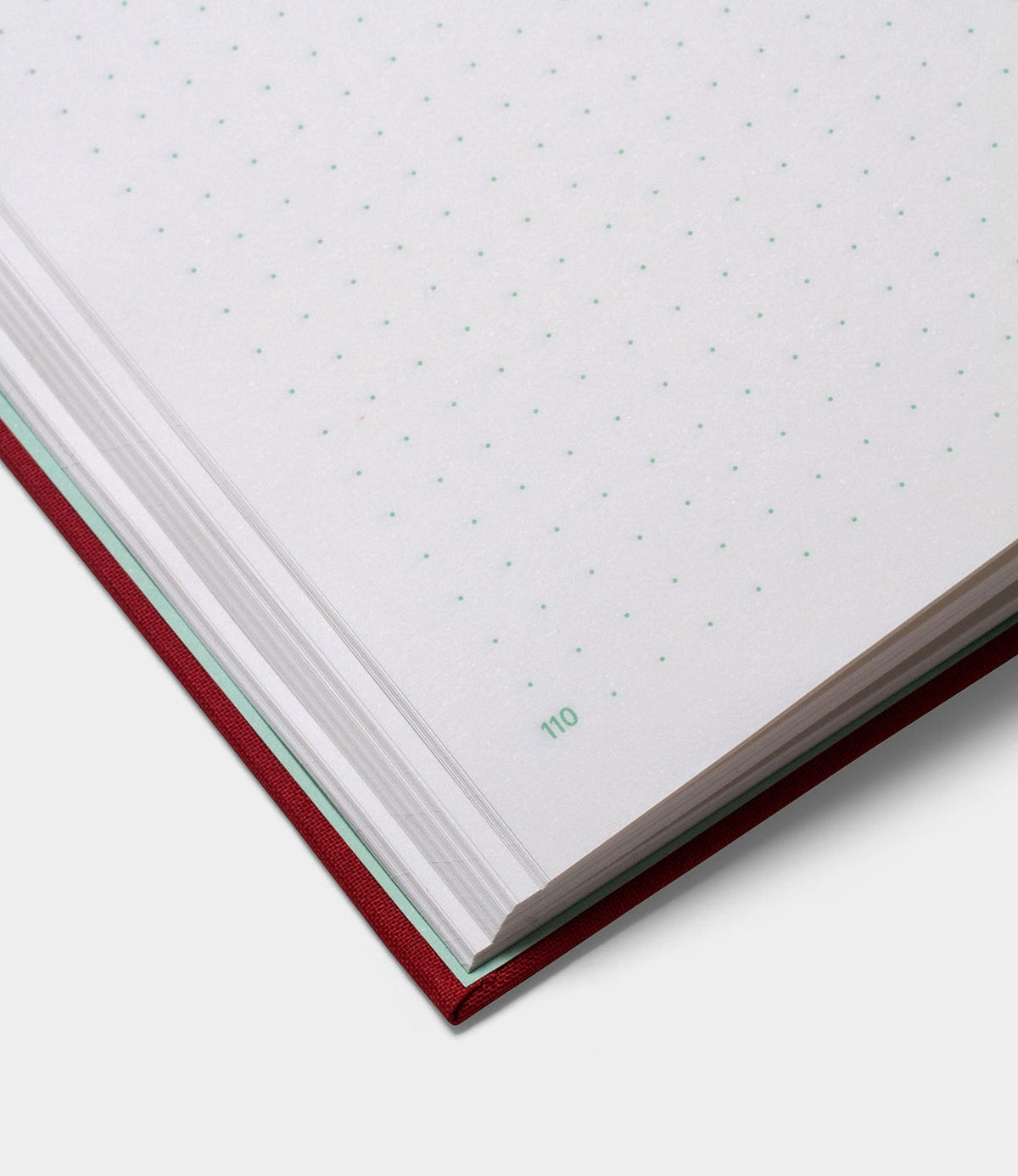 Close-up of the S.B.T. Max Cloth-Bound Notebook by Best Made Co., a red hardcover with white dotted grid pages; corner of page 110 is numbered in green.