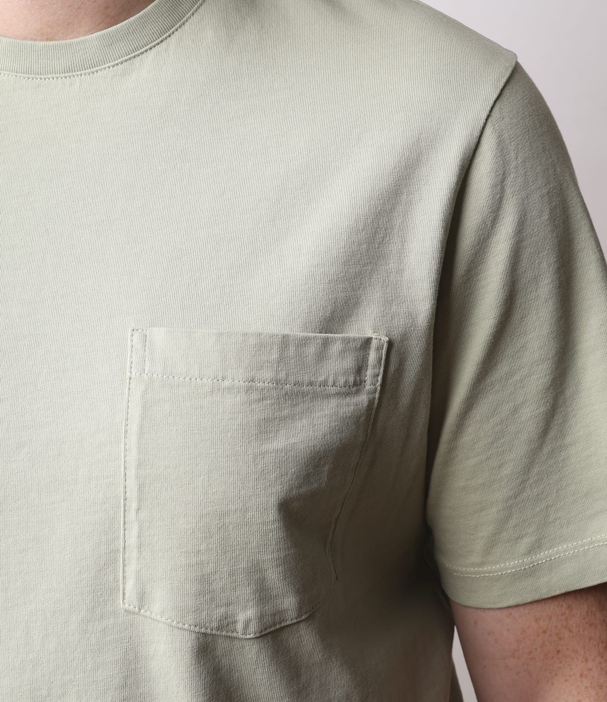 Close-up of someone wearing the Best Made Co. Standard Pocket T-Shirt in Haze, a light green, garment-dyed Peruvian tangüis cotton tee with a left chest pocket. The photo shows the upper torso and part of an arm, not the face.