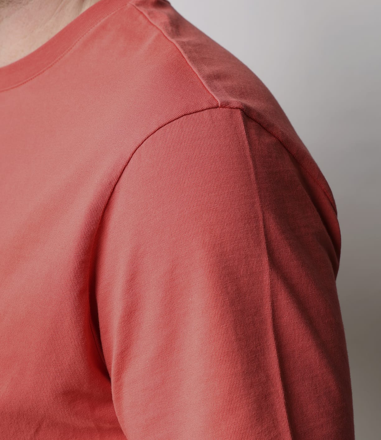 Close-up of a person wearing the Best Made Co. Standard T-Shirt in Faded Red, made from Peruvian tangüis cotton, showing the shoulder, upper arm, and chest against a light gray background. Face and lower body are not visible.