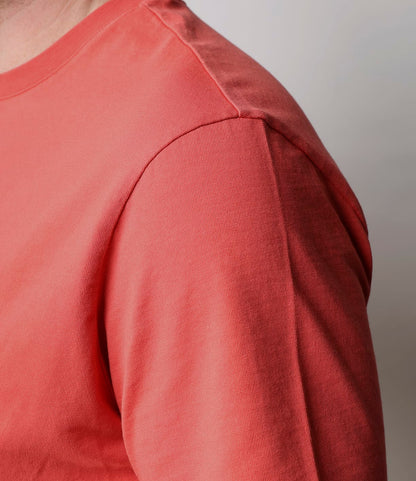 Close-up of a person wearing the Best Made Co. Standard T-Shirt in Faded Red, made from Peruvian tangüis cotton, showing the shoulder, upper arm, and chest against a light gray background. Face and lower body are not visible.