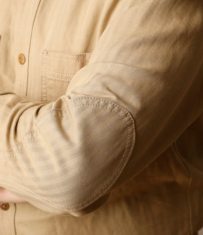 A close-up of a person's arm wearing the Best Made Co. Cotton-Linen Workshirt Tan, featuring an elbow patch and pocket seam detail, made in Portugal.