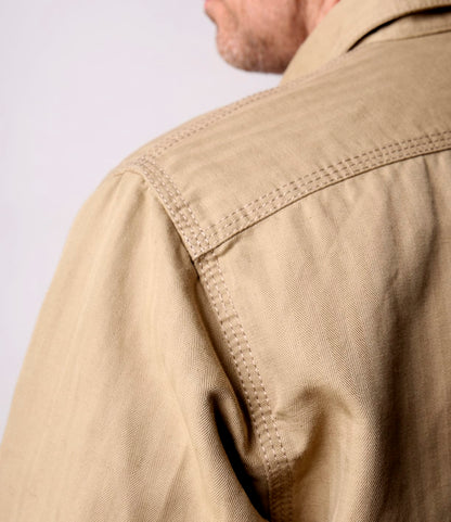 Close-up of a person wearing the Best Made Co. Cotton-Linen Workshirt Tan, highlighting detailed shoulder and upper back stitching. The collared shirt's texture is visible as the wearer’s face is partially turned from the camera.