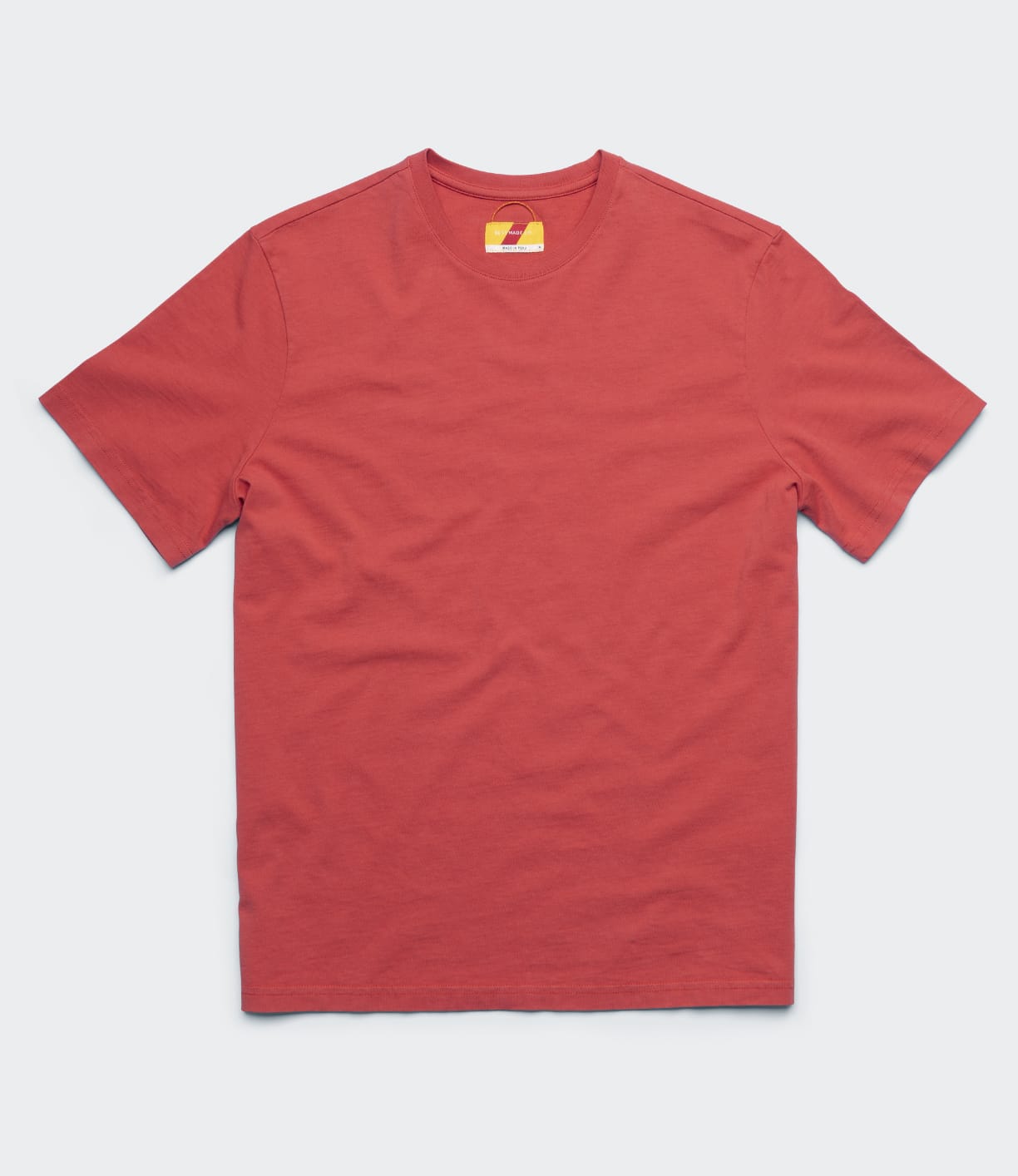The Best Made Co. Standard T-Shirt in Faded Red, a garment-dyed short-sleeve tee with a small yellow and red collar tag, is laid flat on a light gray background—an essential wardrobe staple.
