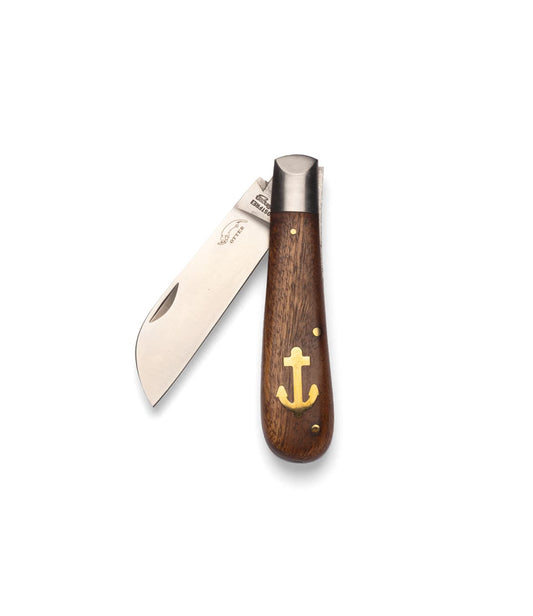 The Best Made Co. Anchor Knife is a folding nautical knife with a partially open sheepsfoot blade and a wooden handle featuring a brass anchor inlay, shown on a plain light gray background.