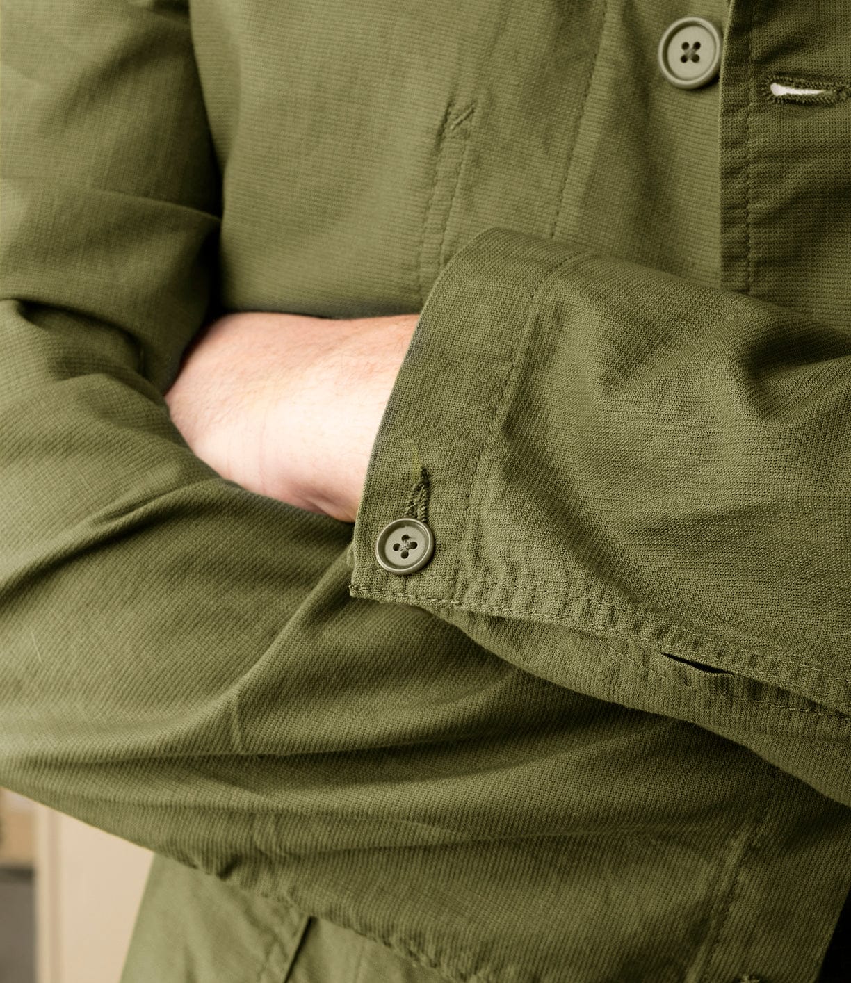 A person with fair skin stands arms crossed, wearing the Best Made Co. Panama Cloth Service Jacket crafted from Japanese cotton. The focus is on the sleeve and buttons, set against a softly blurred neutral background.