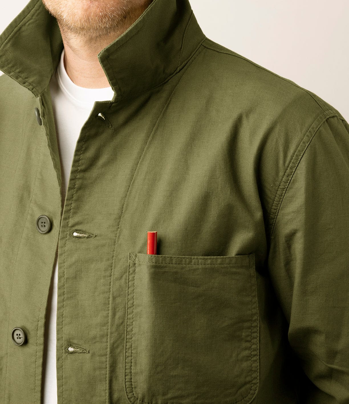 A person wearing a Best Made Co. Panama Cloth Service Jacket in olive green over a white shirt, with a red pen in the chest pocket. The person's face is partially out of frame.