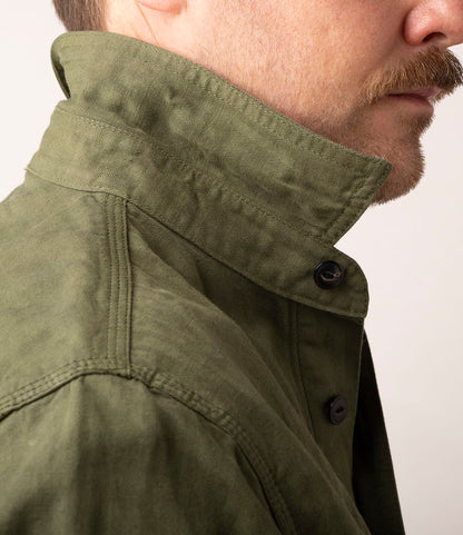 Close-up side view of a light-skinned person with a mustache wearing the Best Made Co. Cotton-Linen Workshirt in Olive Drab, collar turned up, against a plain light background.