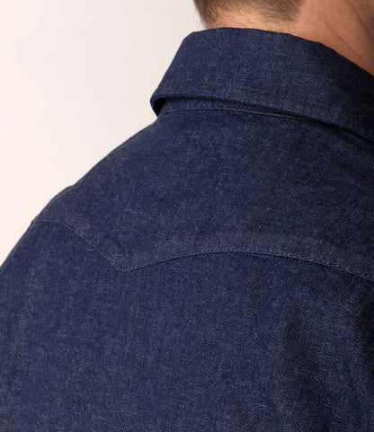 Close-up of a person wearing the Best Made Co. Fukuyama Snap-Front Shirt, crafted from Japanese indigo denim. The image highlights the collar and stitching details on the upper back and neck, with the person's head partially visible and turned away.