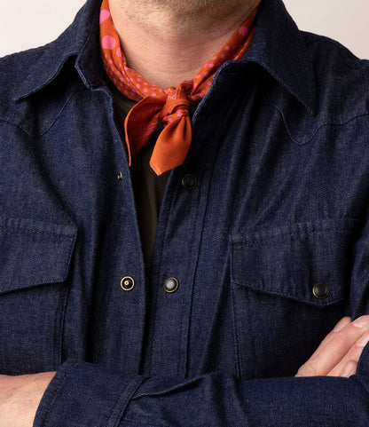 Wearing the Best Made Co. Fukuyama Snap-Front Shirt in dark Japanese indigo denim, paired with an orange scarf with pink polka dots tied at the neck, arms crossed and face partially out of frame.