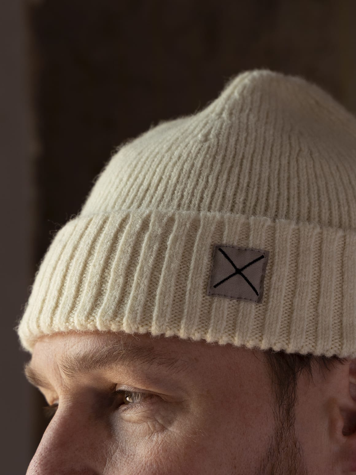 Best Made Co. Shetland Cap of Courage: a cream-colored ribbed knit beanie made of undyed Shetland wool, featuring a square patch with an X embroidery on the cuff.