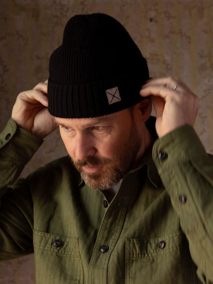 A man adjusting a black lambswool Cap of Courage featuring a small square patch with an X on the cuff.