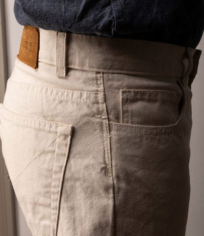 A close-up side view of a person wearing Best Made Co.'s Standard 5-Pocket Pant M2 Undyed, highlighting the pocket, belt loop, and brown leather patch on the waistband.