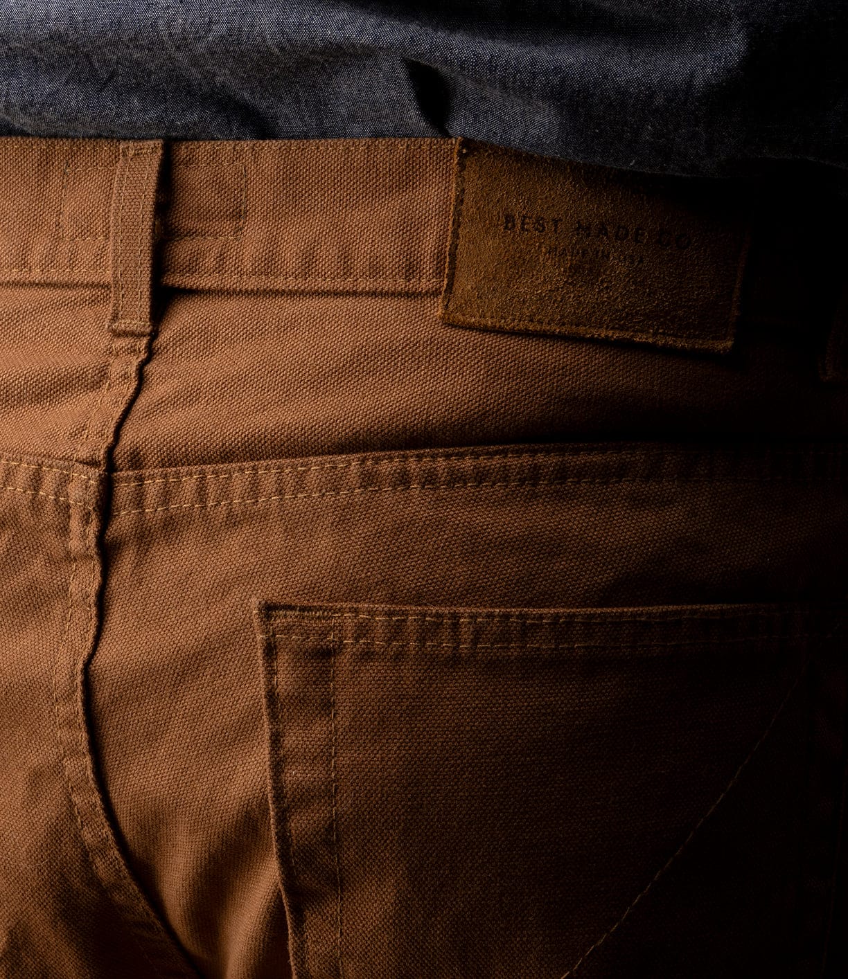 Close-up of Best Made Co Standard 5-Pocket Pant M2 Field Brown in heavyweight cotton with visible stitching, belt loops, and leather patch on the waistband. Shown with a dark shirt tucked in.