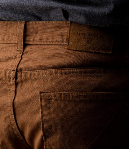 Close-up of the back of a person wearing Best Made Co. Standard 5-Pocket Pant M2 Field Brown, featuring visible stitching, a leather patch on the waistband, and a dark gray shirt tucked in.