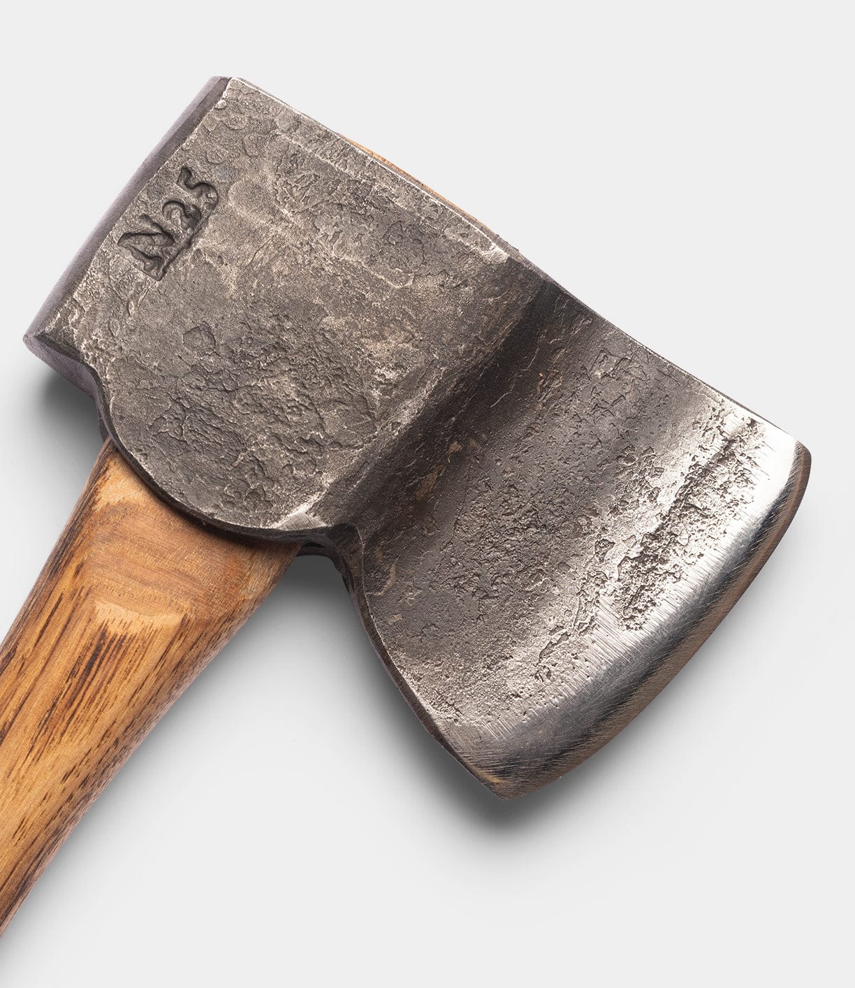 Close-up of the Spark (Straight-Hold Edition) axe head by Best Made Co., crafted from weathered high-carbon steel with N25 engraving, affixed to a smooth Appalachian hickory handle against a plain light background.