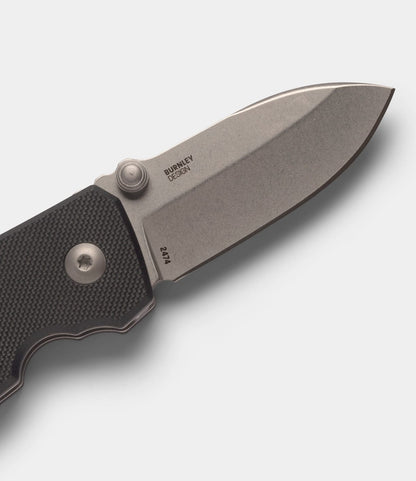 A close-up of the CRKT Squid pocket knife by Best Made Co. shows its textured black handle and D2 steel blade with Burnley Design engraving, partially open with a button lock against a plain light background.