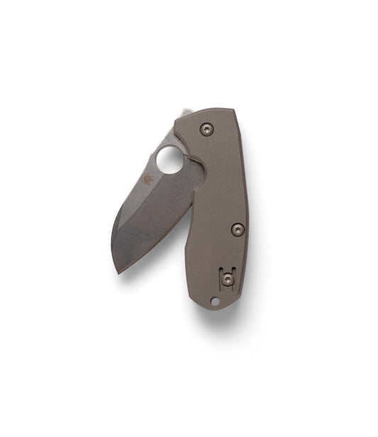 Someone sharpens a Best Made Co Spyderco Techno 2 pocket knife (CTS-XHP steel) on a whetstone, holding the blade against the stone with both hands. Everything is set up on a green cutting mat featuring measurement markings.