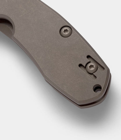 Close-up of the matte-finished handle on the Best Made Co. Spyderco Techno 2 titanium framelock pocket knife, showing two screws and extra slots for adjustable pocket clip placement. The surface features a slight texture.