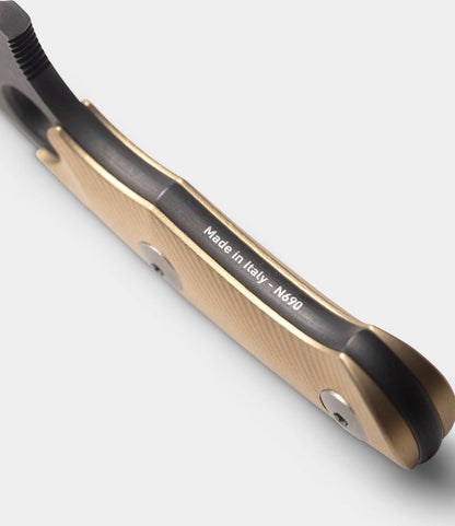 Close-up of a Best Made Co. GiantMouse GMF1-P (BMC Edition) knife handle in tan metallic finish, engraved with Made in Italy - N690. Part of the blade appears on the left, set against a light gray background.