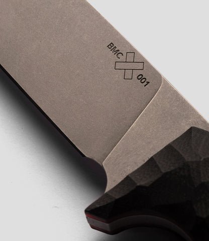 Close-up of a NWBW Field Knife (BMC Edition) blade by Best Made Co., showing the engraving "BMC 001" with a cross symbol and part of its black textured handle against a light gray background.