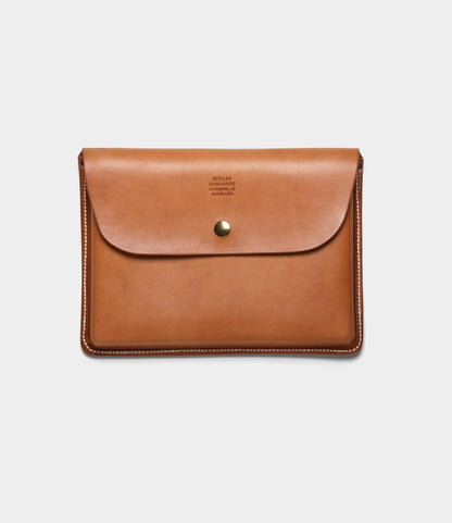 The Best Made Co. Gfeller Case Small is a tan leather envelope-style document case with white hand-stitched edges, a brass button closure, and minimal text embossed near the top center.