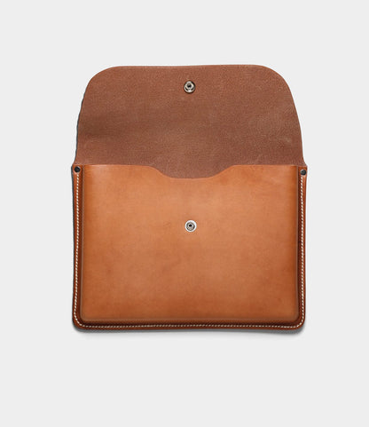 A small tan Gfeller Case by Best Made Co. in envelope style, flap open to reveal suede interior and snap button closure, highlights the elegance of this hand-stitched leather accessory against a plain white background.